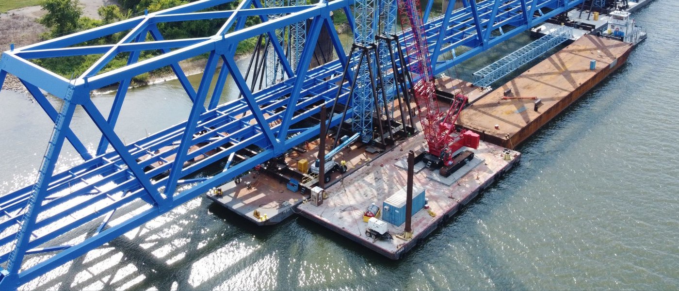 Blue truss bridge under construction over a river